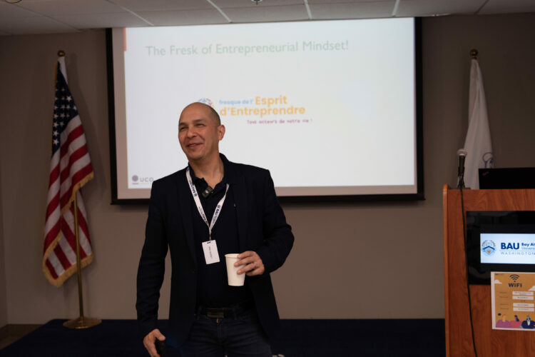 Person speaking at entrepreneurial mindset seminar with presentation slide and flags in background.