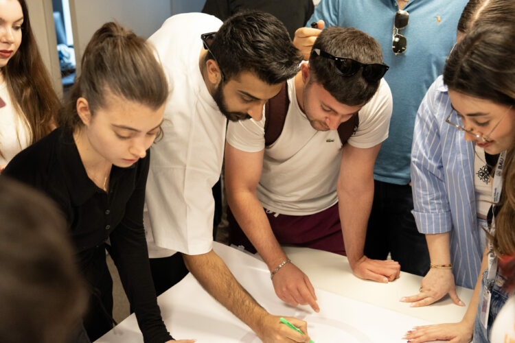 Group of young adults collaborating on a project, gathered around a table, pointing at and discussing a plan.