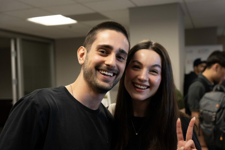 Smiling friends posing together, one showing a peace sign at a social event indoors.