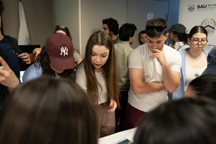 Group of people engaged in discussion around a table at an event, with university logo in the background.