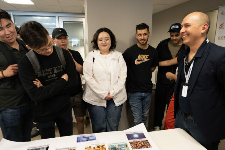 Group of people gathered around a table viewing a presentation or project in an office setting.