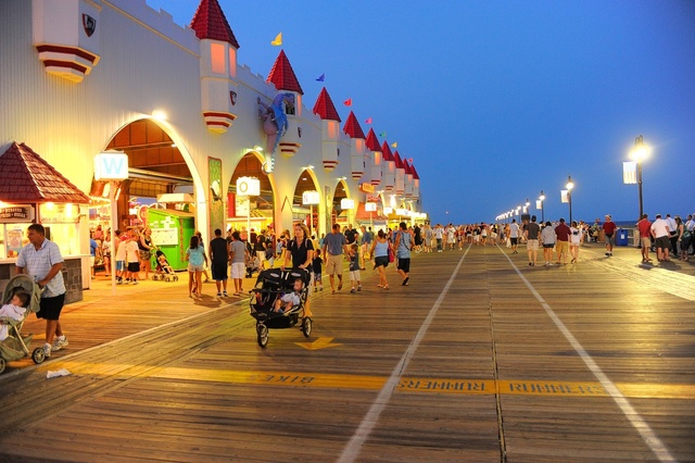 People strolling on a vibrant beach boardwalk in the evening with shops and colorful lights.