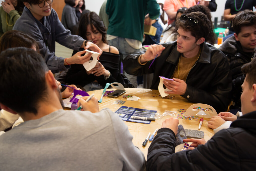 KQ9A8133 People decorating masks at a creative workshop table with craft supplies and colorful stickers.