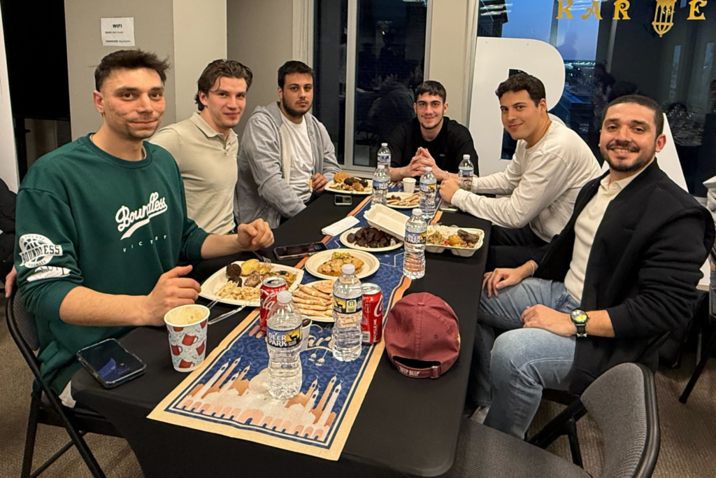 Untitled design (27) Group of friends enjoying a meal together at a table, with drinks and food in a casual setting.