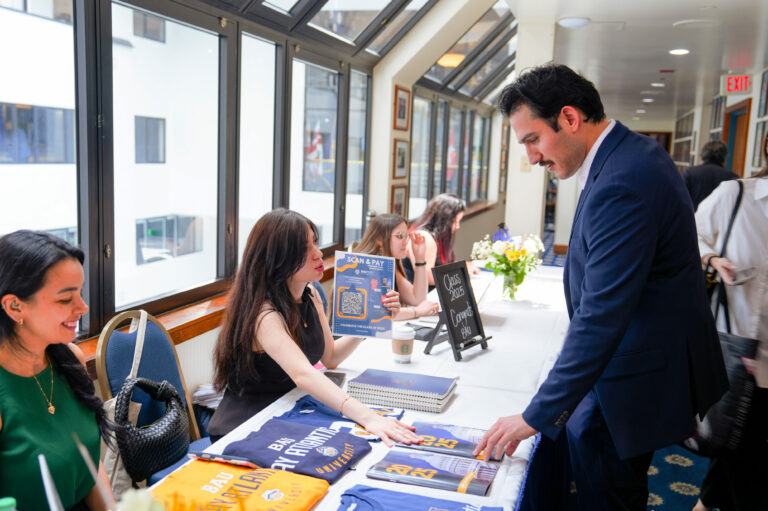 Man at a university merchandise table, interacting with attendants showcasing products and promoting mobile payments.