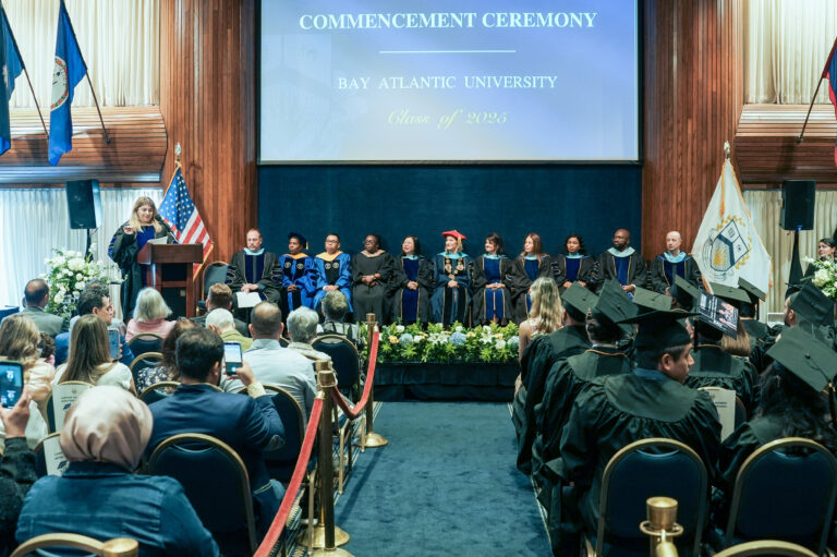 Graduation ceremony at Bay Atlantic University, Class of 2025, featuring students and faculty on stage.