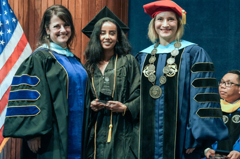 Graduate receives award at university ceremony with faculty in academic regalia.