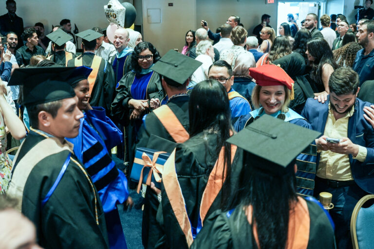 Graduates in caps and gowns celebrate with faculty and friends at a crowded graduation ceremony.