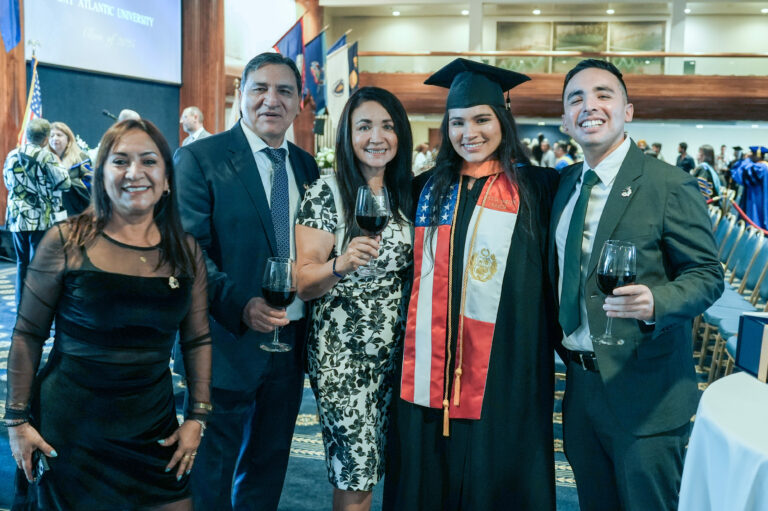 Graduation celebration with friends and family holding wine glasses, smiling graduate in cap and gown.