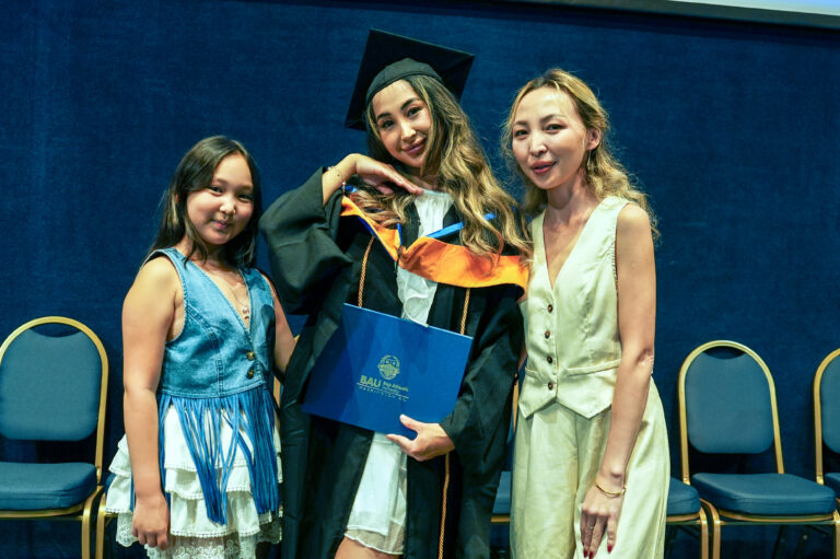 Graduate posing with family at a graduation ceremony, holding a diploma and wearing a cap and gown.