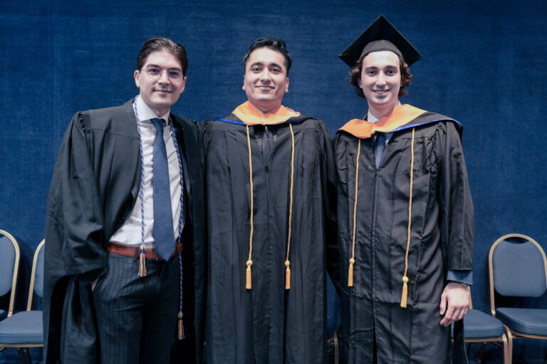 Three graduates in caps and gowns smiling at a ceremony, celebrating their achievements together.