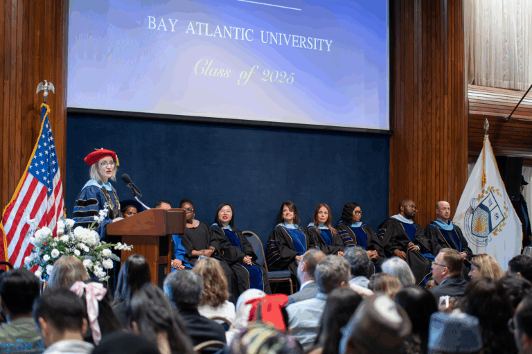 Graduation ceremony at Bay Atlantic University, Class of 2025, with faculty on stage and audience attending.