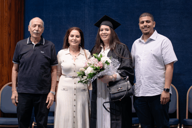 Family celebrates graduation with smiles, flowers, and a cap and gown against a blue backdrop.