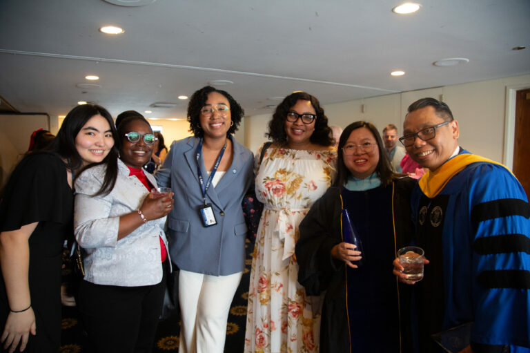 Group of diverse professionals smiling at a formal event, with one person wearing academic regalia.