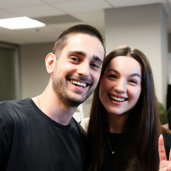 Smiling friends at a casual gathering, one showing a peace sign, indoors.
