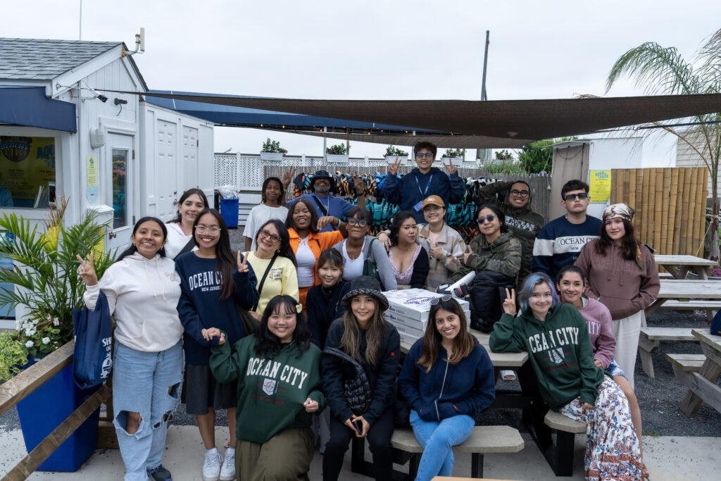 252-DSC00700 Group of friends smiling and posing at an outdoor event with benches and greenery in the background.