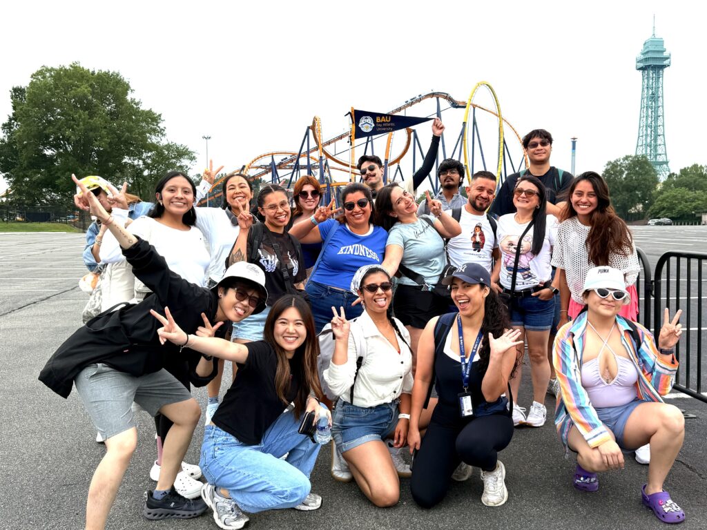 IMG_E4806 Group of friends smiling and posing at an amusement park with roller coaster in the background.
