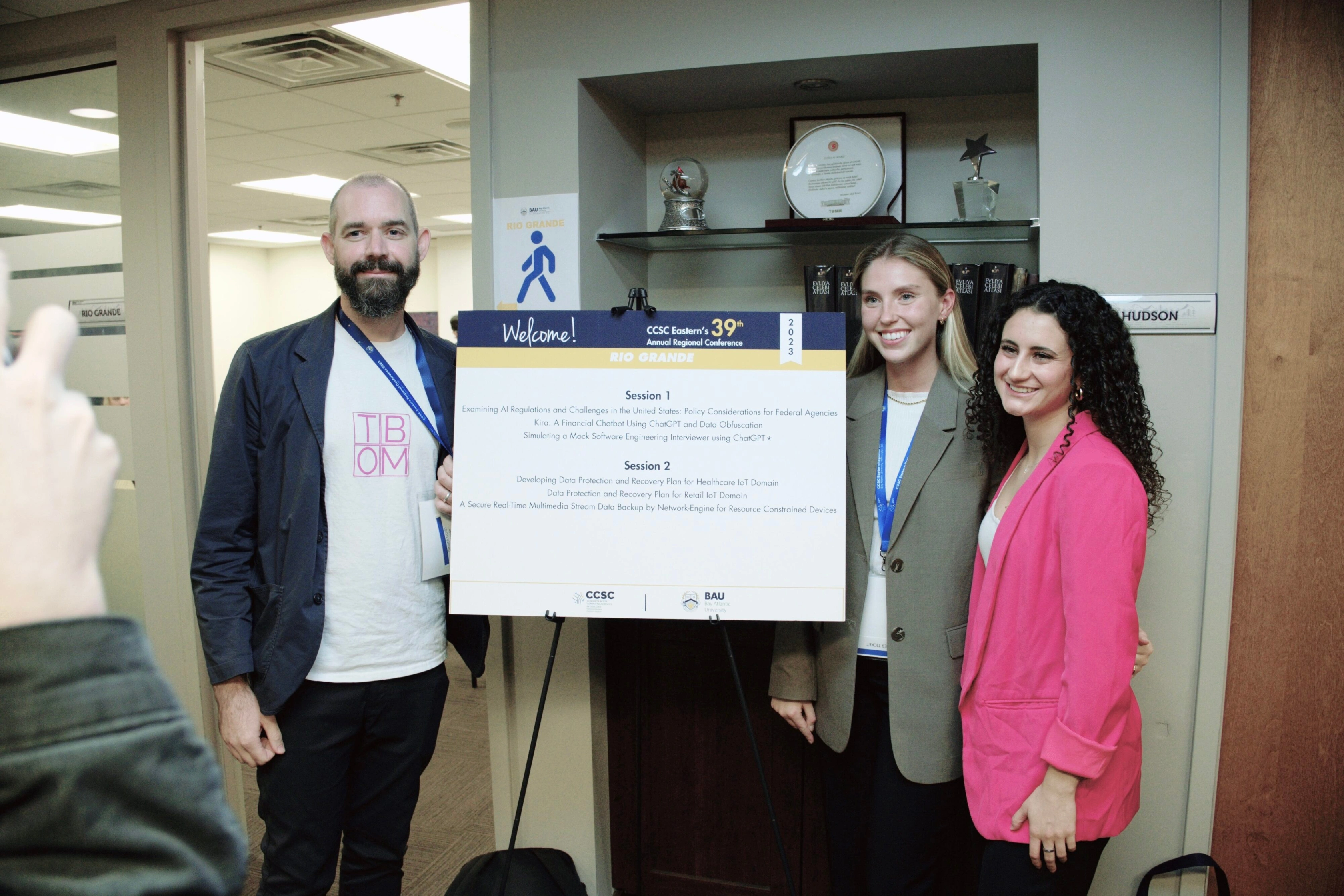 Three people smiling beside a conference poster at CCSC Eastern's 39th Annual Regional Conference, 2023.