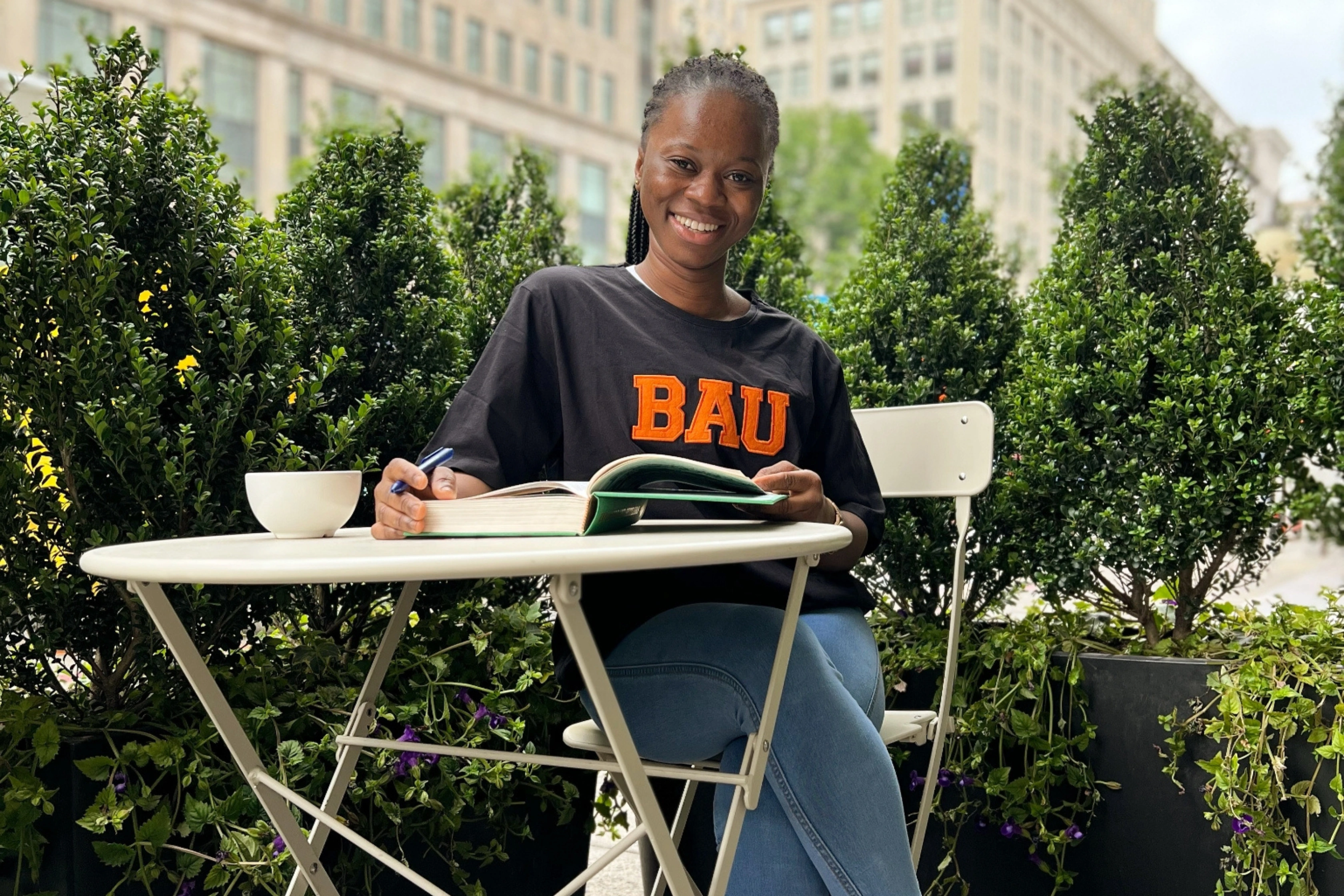 Person studying in a garden café while smiling, wearing a BAU shirt.