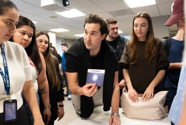 Group of students discussing a project around a table, man holding a booklet titled The Purpose.