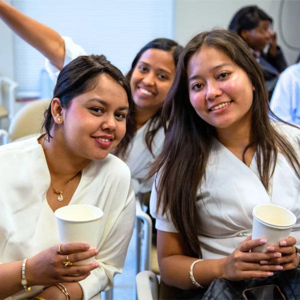 Three women smiling with coffee cups in a casual meeting setting.