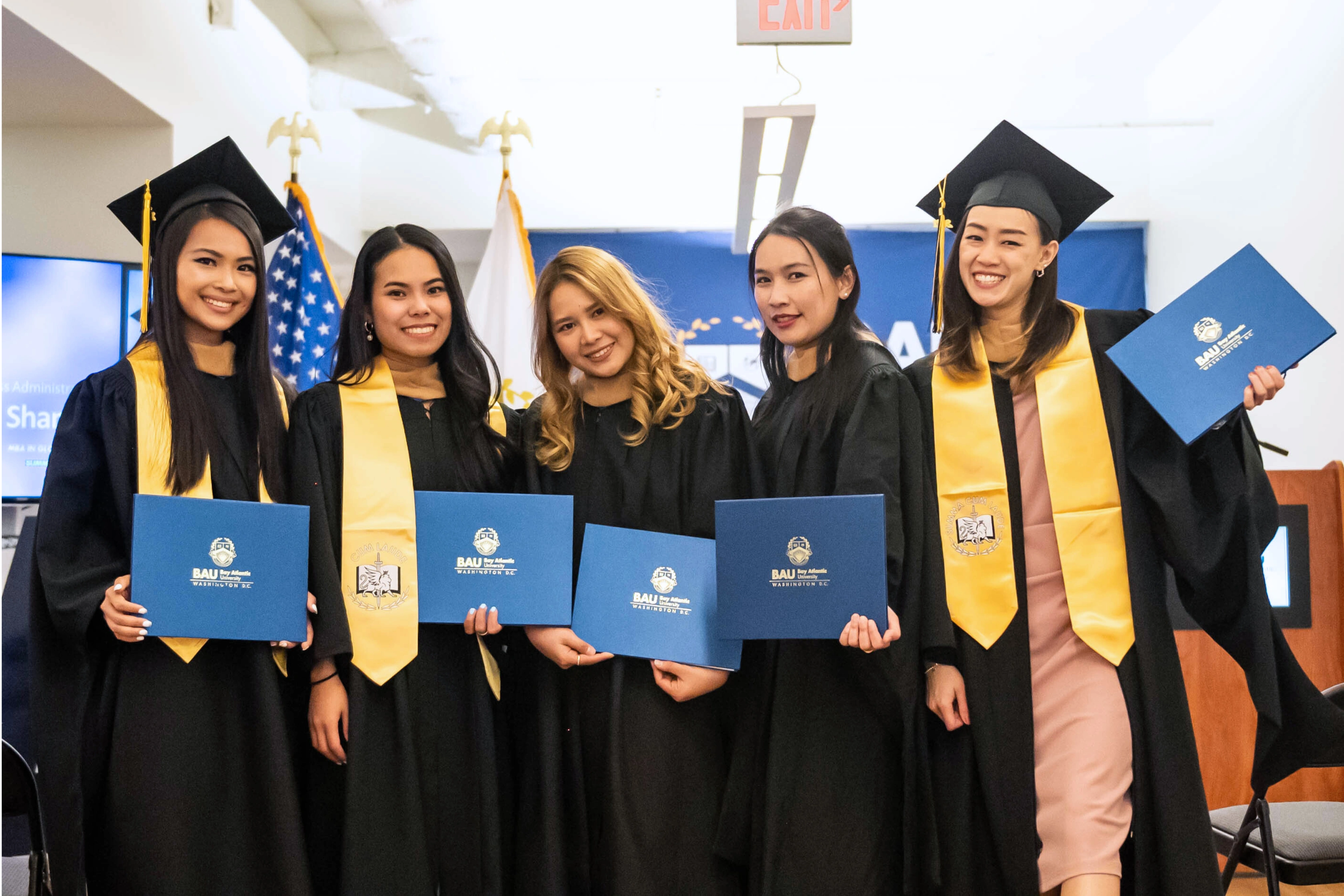 Five graduates in caps and gowns proudly holding diplomas, celebrating their academic achievement.