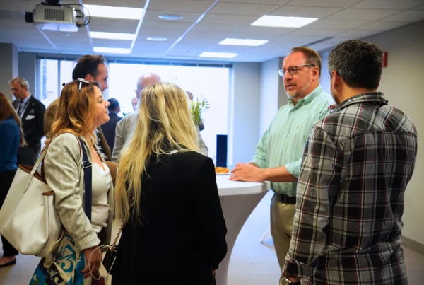 People networking at a professional event around a standing table in an office setting.