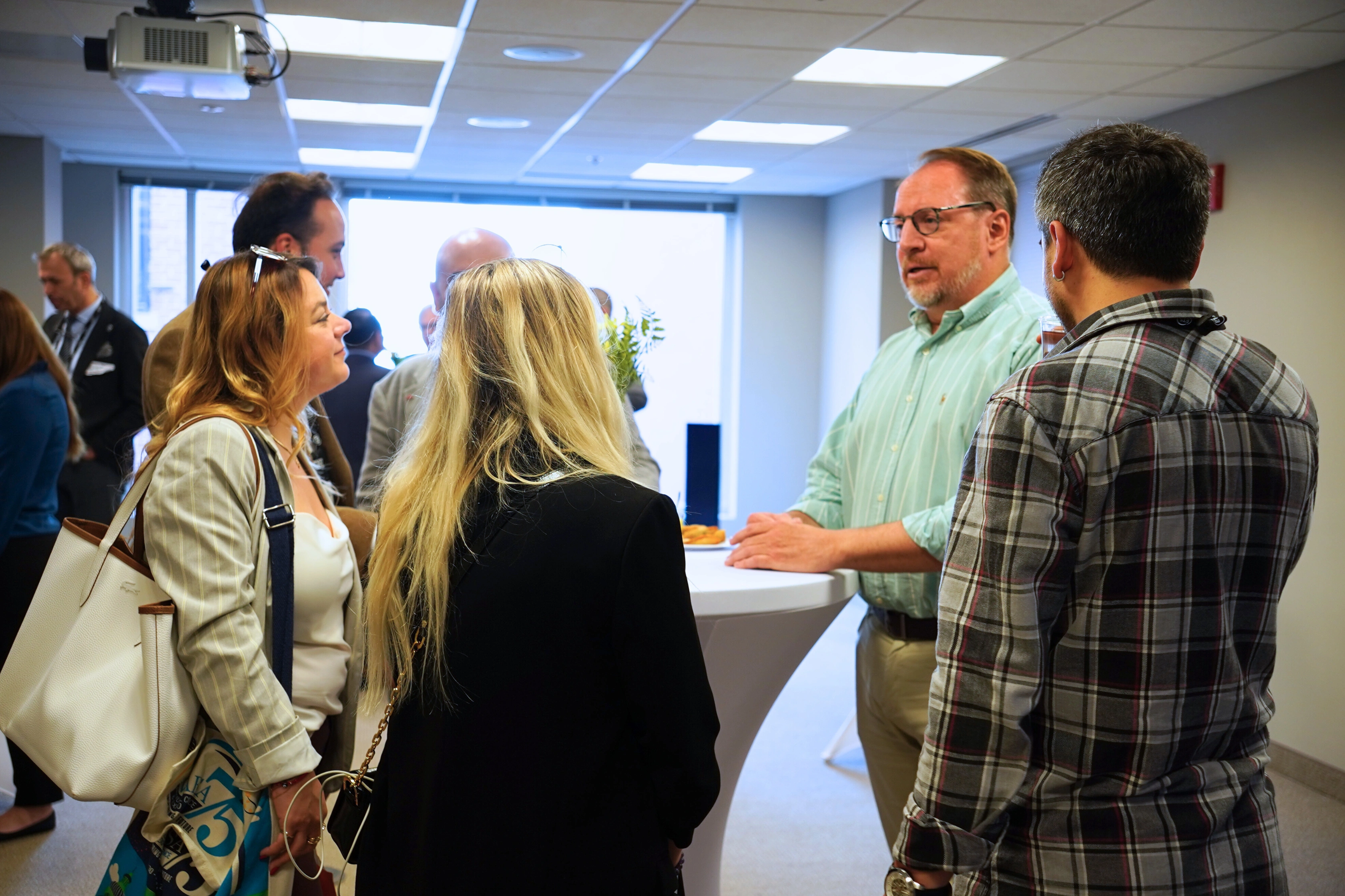 People networking at a professional event around a standing table in an office setting.