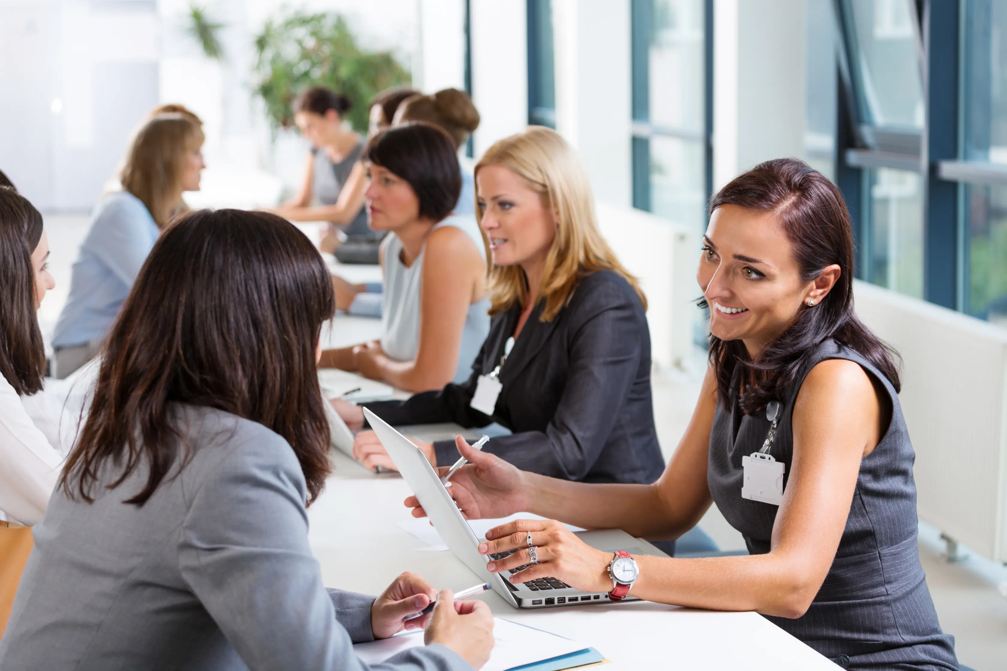 Business professionals engaged in a speed networking event, discussing and exchanging ideas at a long white table.