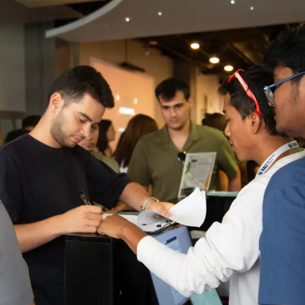 People registering at an event, discussing and filling out forms at a reception desk.