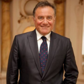 Smiling man in a suit and tie standing in an elegant room with ornate decor, exuding confidence and professionalism.
