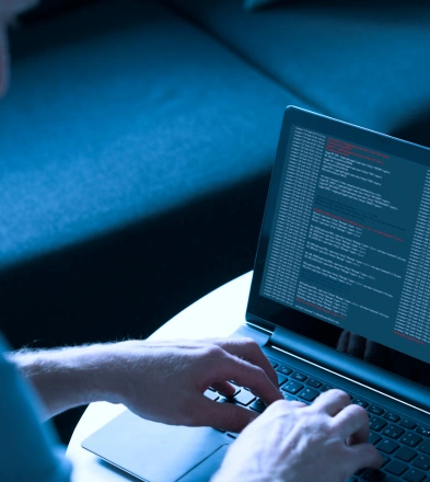 Person coding on a laptop with text editor, bright screen, and blue hue. Tech work and programming concept.