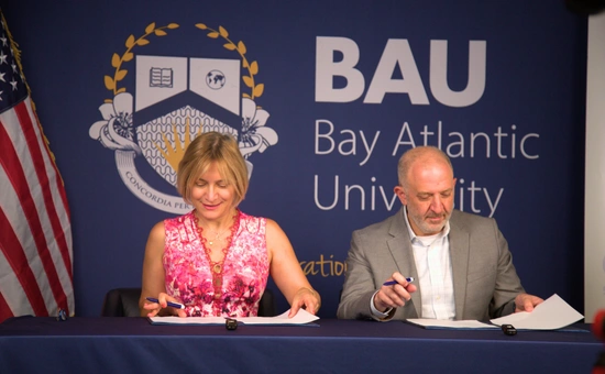 Two people sign documents at Bay Atlantic University with a logo backdrop.