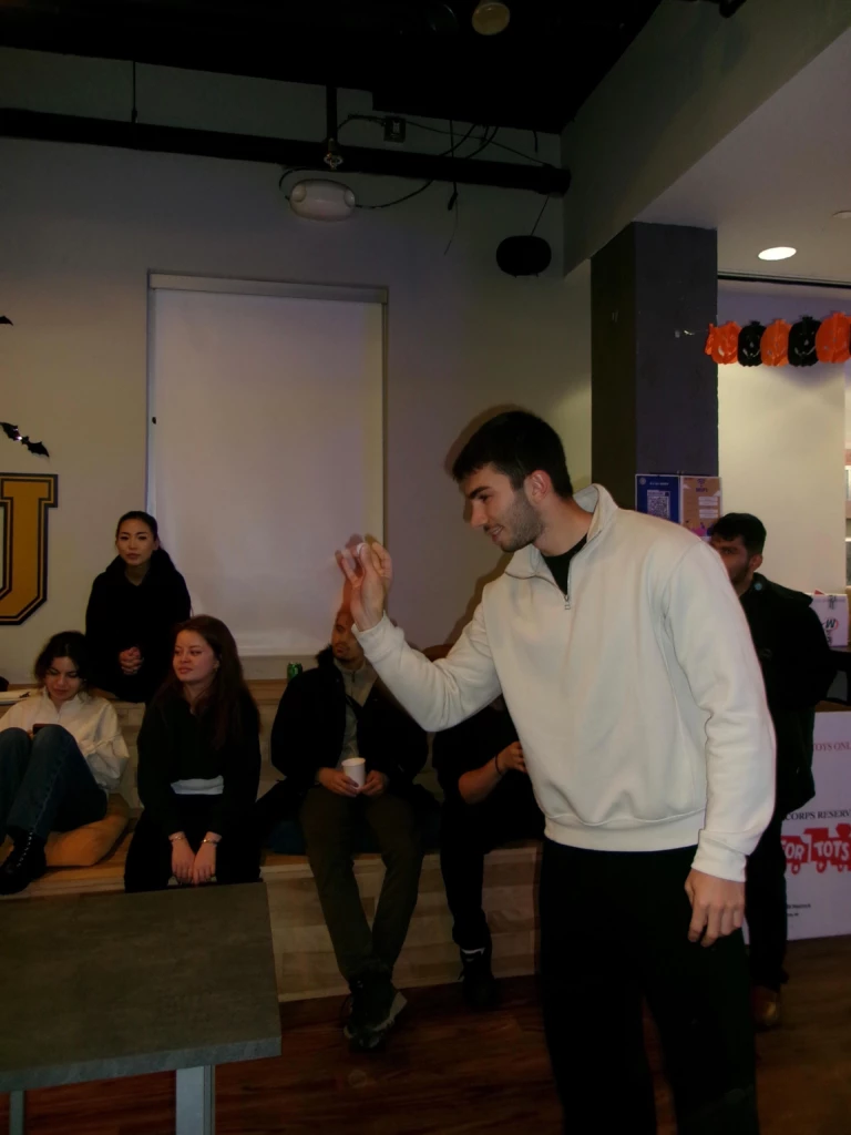 SGA Halloween Party 2025 Man playing game with focused group watching in casual indoor setting.