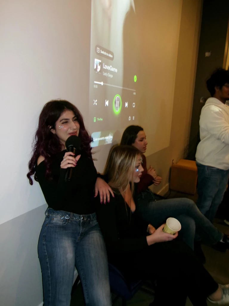 SGA Halloween Party 2025 Group enjoying karaoke night with music on screen in background.