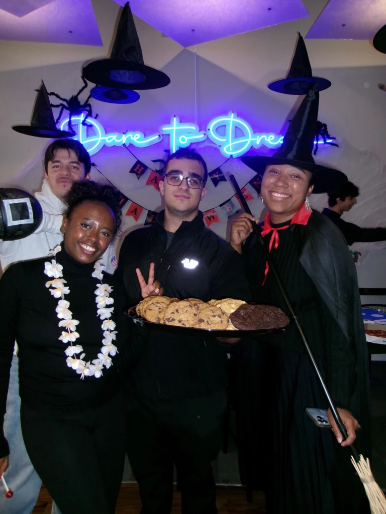 SGA Halloween Party 2025 Group in Halloween costumes with cookies under neon sign Dare to Dream.