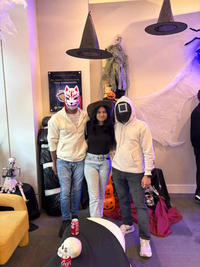SGA Halloween Party 2025 Three people in Halloween costumes posing joyfully at a festive event with spooky decorations including witches' hats.