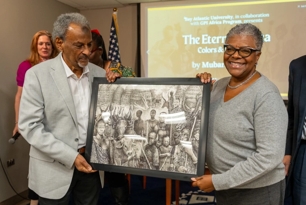 Two people holding an African-themed framed artwork at a university event presentation.