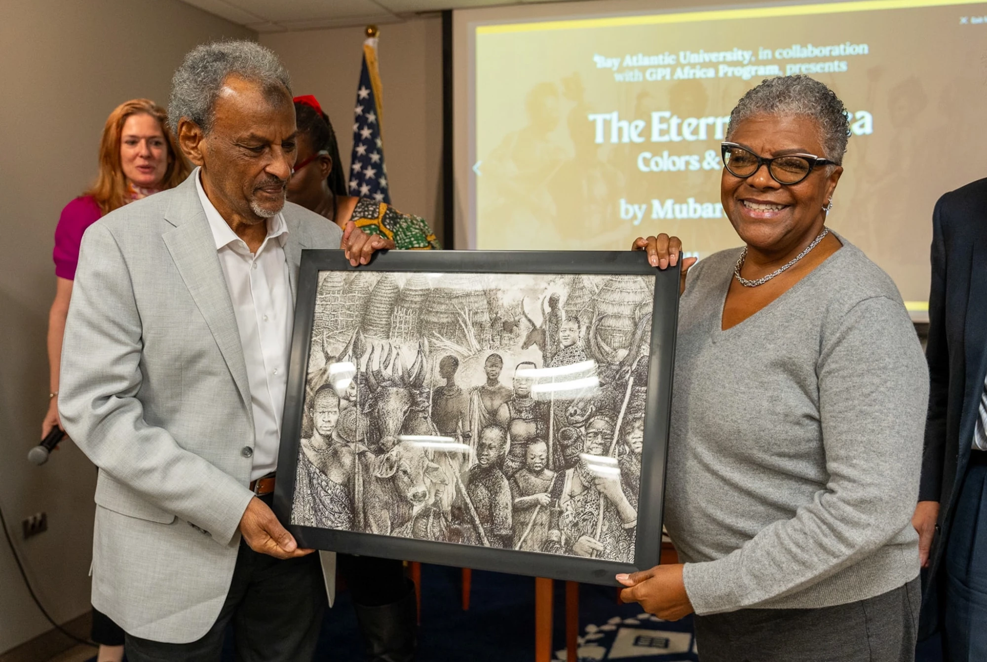 Two people holding an African-themed framed artwork at a university event presentation.