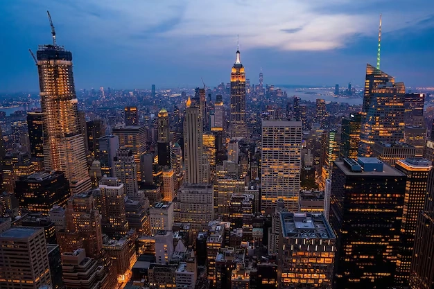 Skyline of New York City at dusk with illuminated skyscrapers and a deep blue sky, showcasing urban architecture.