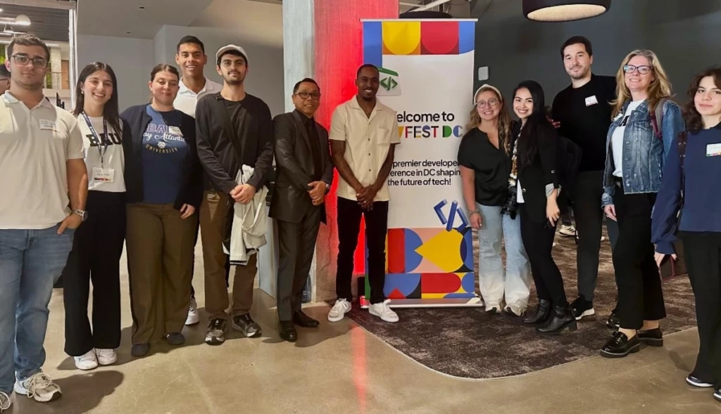 Group of people standing by a colorful banner at DevFest DC, a tech conference event.