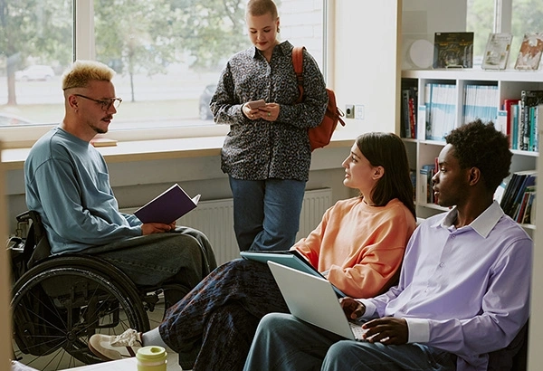 Group of diverse students studying together in a library, with one in a wheelchair.