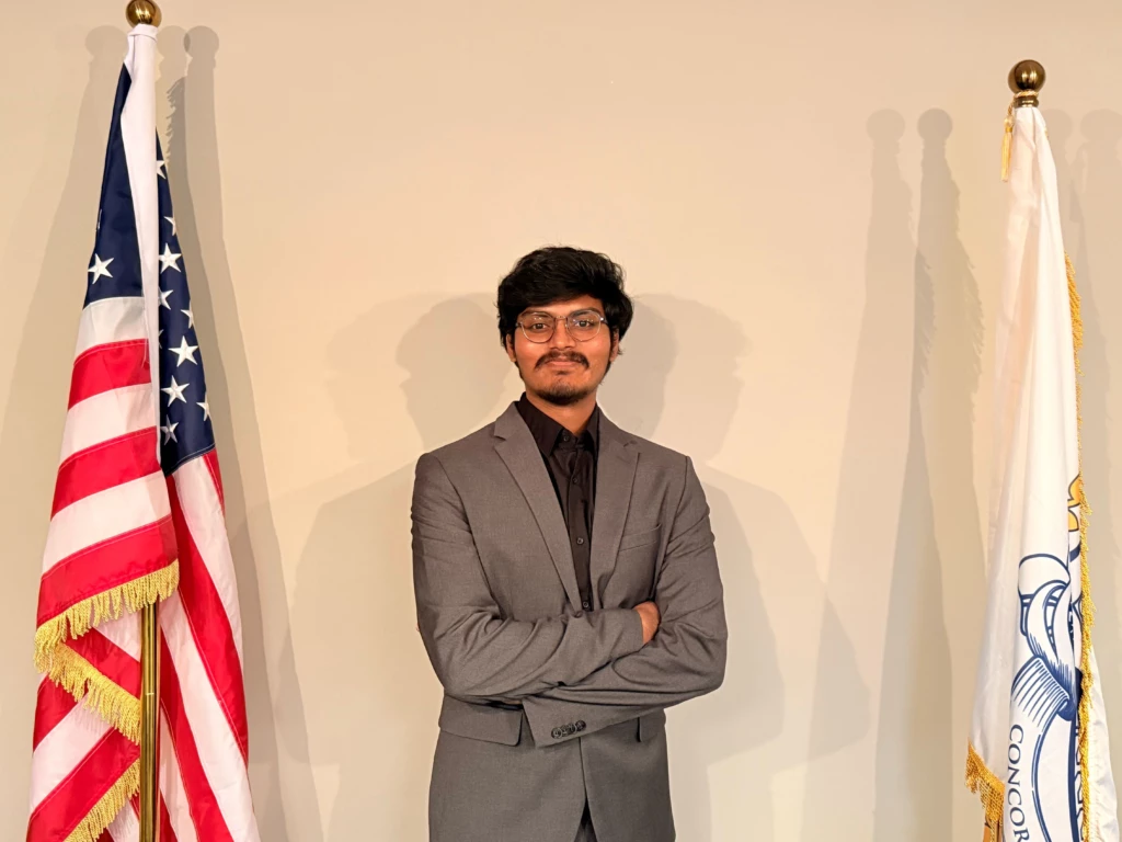 Tech Connect Event with Student Government Association 2025 Man in gray suit poses between two flags, arms crossed, in a formal setting.