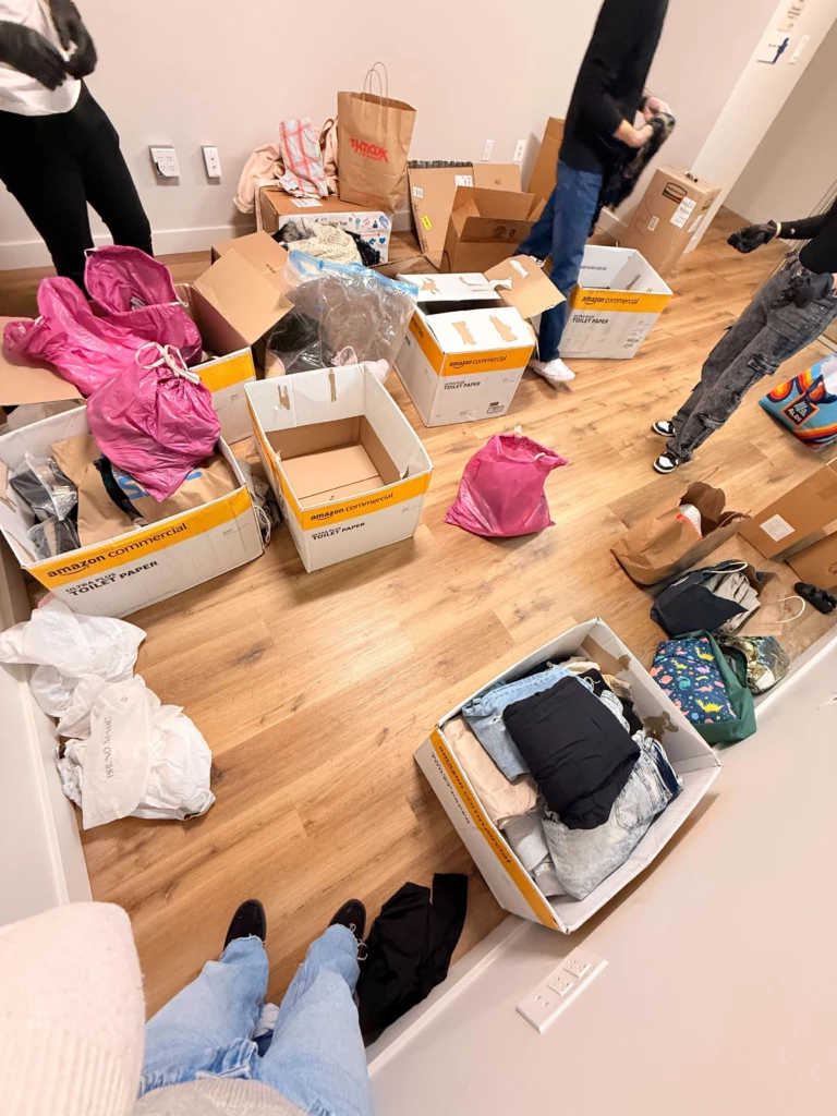SGA Clothing Donations 2025 People sorting clothes and boxes on a wooden floor, preparing for moving or organizing a room.