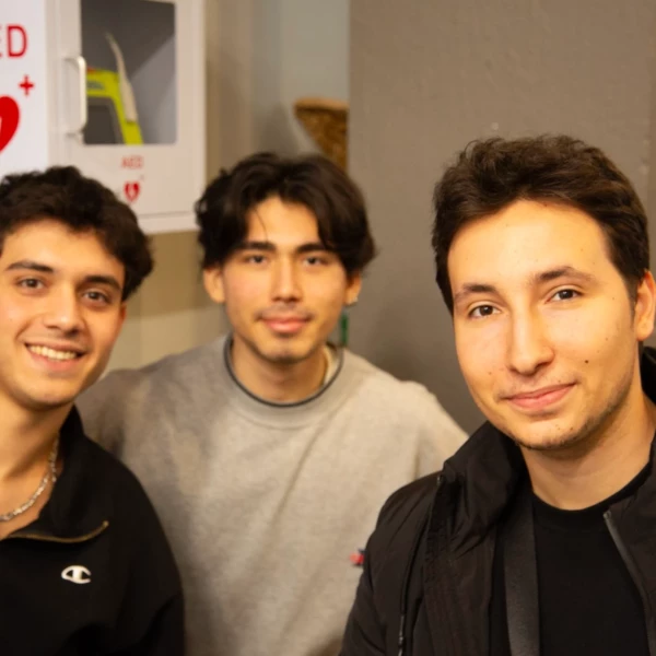 Three friends smiling near an AED machine in a casual indoor setting.