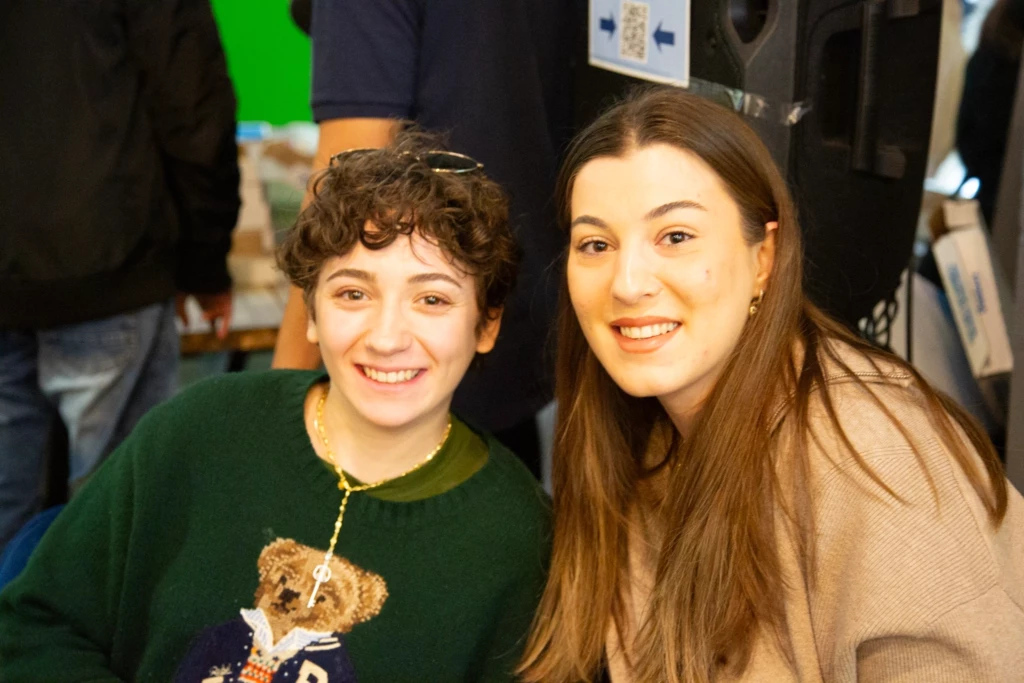 Two people smiling at a social event, wearing casual clothing, with a vibrant background.