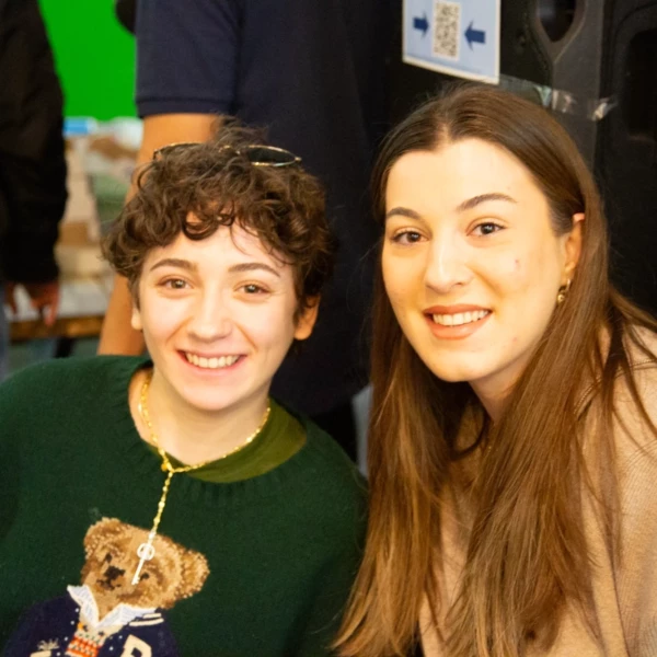 Two people smiling at a social event, wearing casual clothing, with a vibrant background.