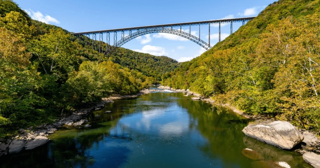 Suspension bridge over a scenic river in a lush green valley, under a clear blue sky.
