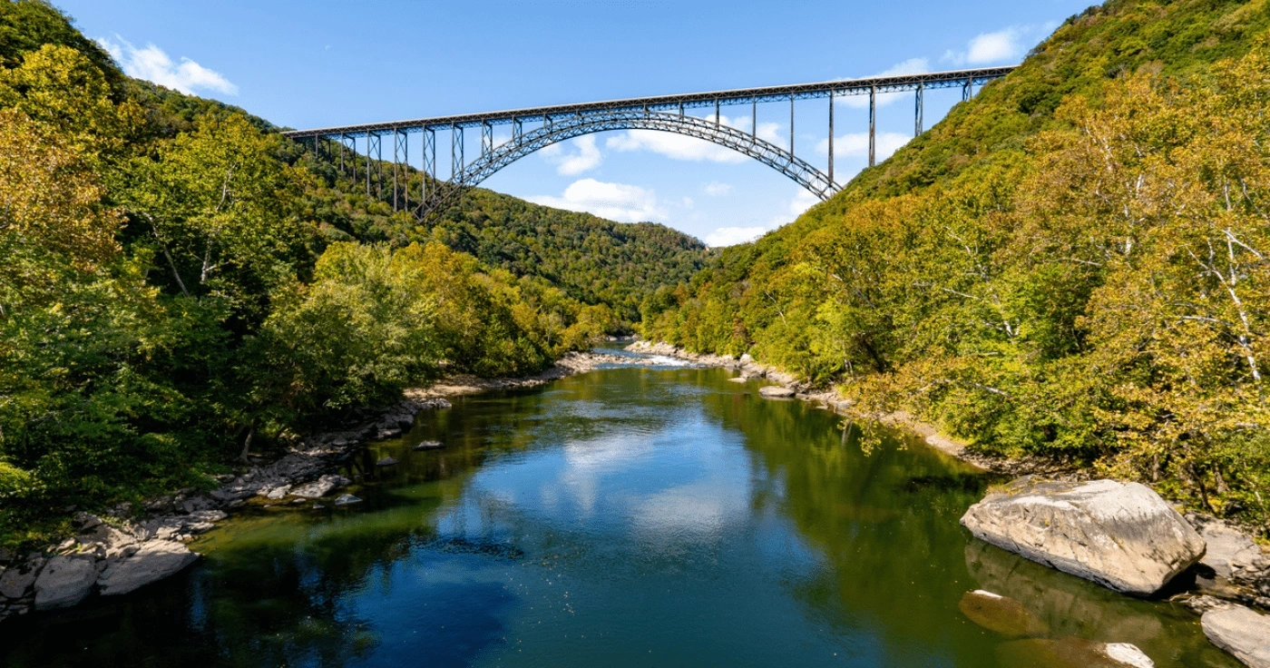 Suspension bridge over a scenic river in a lush green valley, under a clear blue sky.
