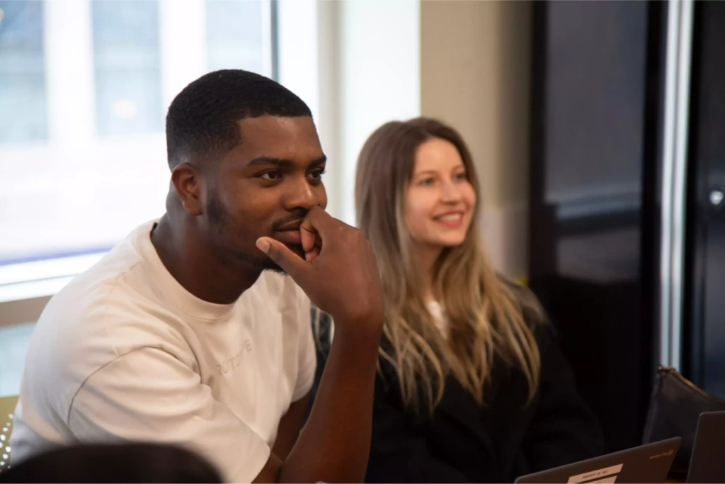 Two people engaged in a professional meeting, one pondering and the other smiling in a bright office setting.